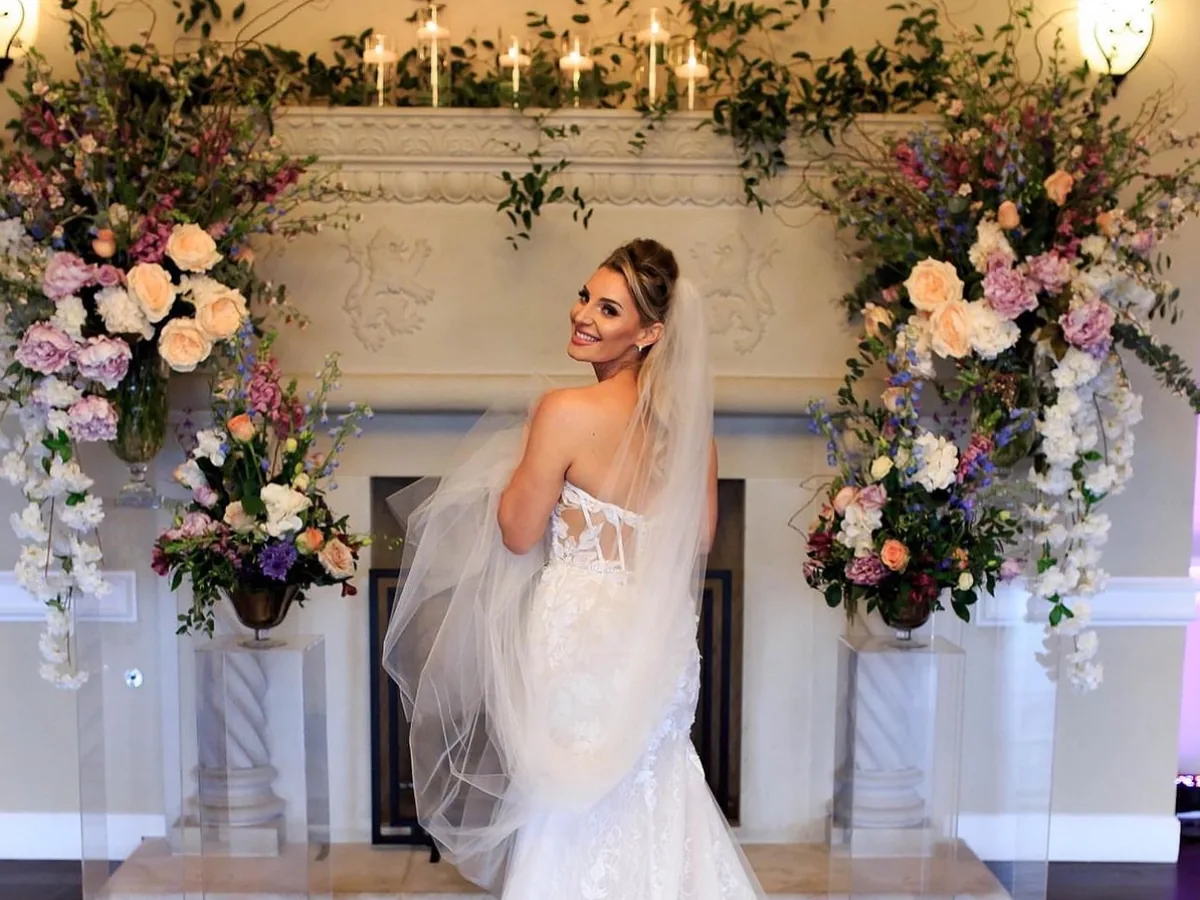 Bride with bridal hair and makeup by Andreina at a DFW wedding floral arch